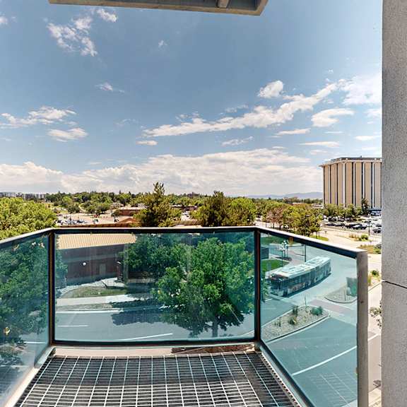 a balcony with a glass railing overlooks city and a green landscape.