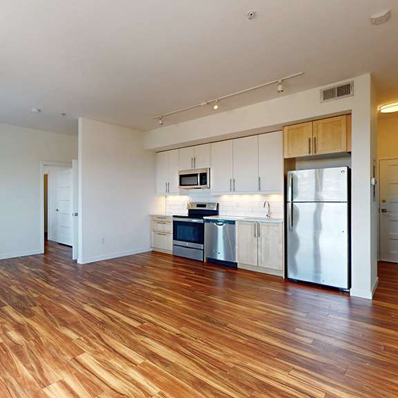 a kitchen with white cabinets and a refrigerator is visible from a living room.