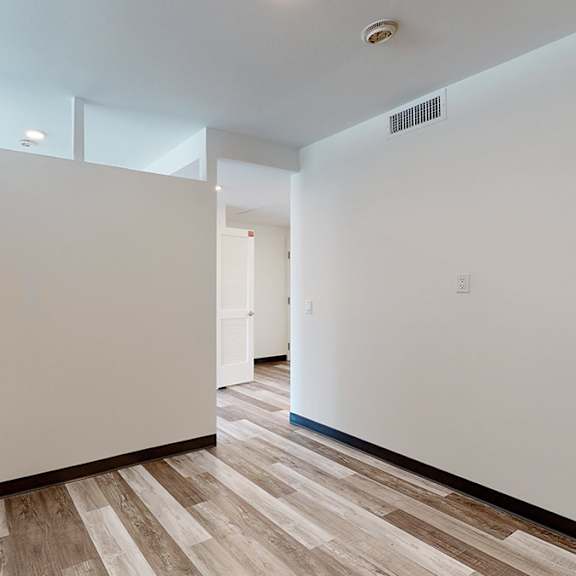 a room with white walls and wooden flooring with a door on the left.