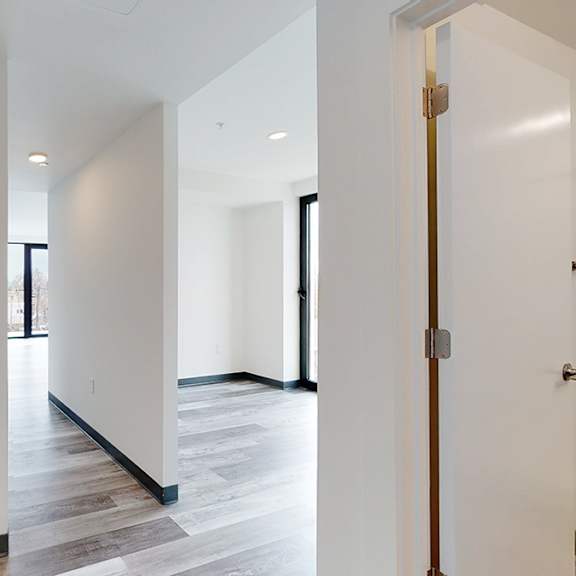 a white hallway with a wooden floor and a door on the right.