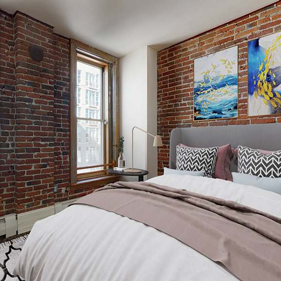 a bedroom with a large bed and an exposed brick wall with 2 large floor-to-ceiling windows.