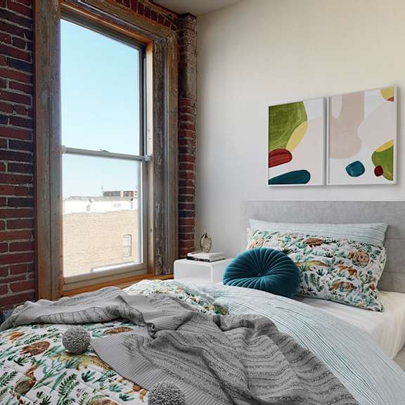 a bedroom with a bed, a nightstand, and a large floor-to-ceiling window. exposed brick wall..