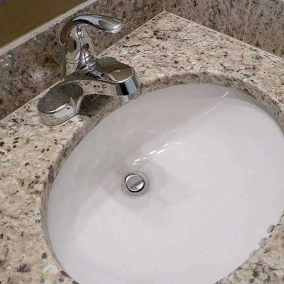 a white sink with a chrome faucet on a granite countertop.