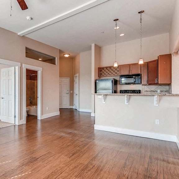 a spacious living room with hardwood floors and a kitchen area in the background.