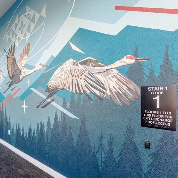 a mural of a bird flying over a forest is on the wall of a room.
