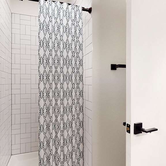 a white bathroom with a shower curtain and a black door.