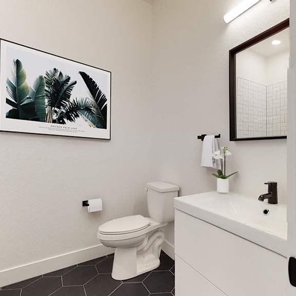 a bathroom with a toilet, sink, and a framed picture of a plant on the wall.