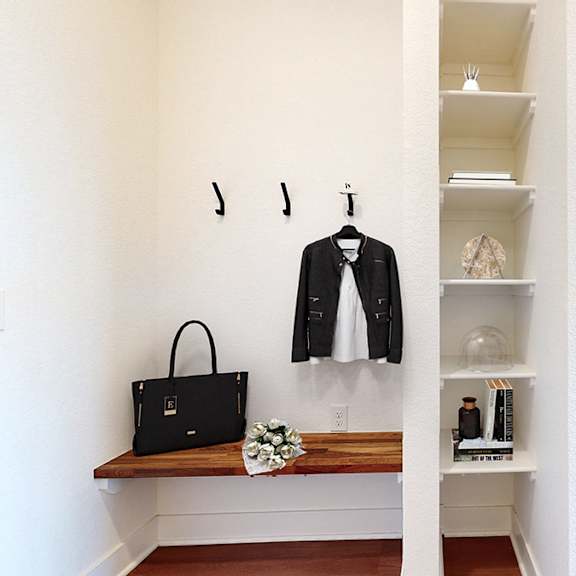 a black handbag sits on a bench next to a black coat hanging on a coat rack.