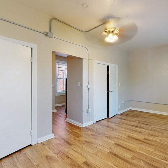 a room with wooden floors and white walls, with a door on the left and a window in the distance.
