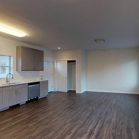 a spacious room with wooden floors and a kitchen area with white cabinets and appliances.