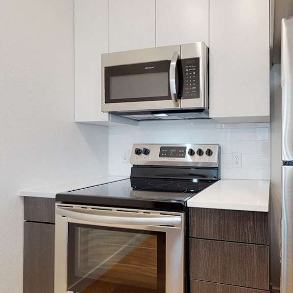 a modern kitchen with a stainless steel refrigerator, microwave, oven, and cabinetry.