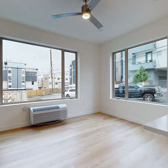 a room with a ceiling fan and two windows overlooking a street.