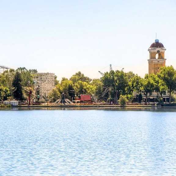 a serene lake with a roller coaster and a tower in the background.