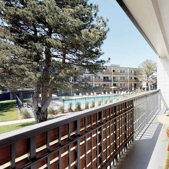 a balcony with a chair and a table is overlooking a pool.
