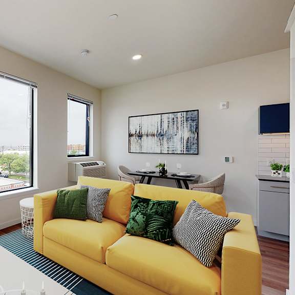 a yellow couch with green and black pillows sits in a room with a large window.