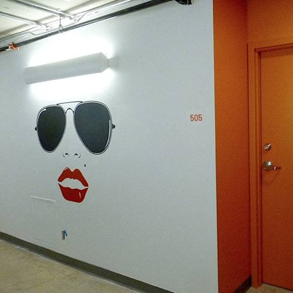 a white wall with a drawing of a woman's face and a door with the number 505 on it.