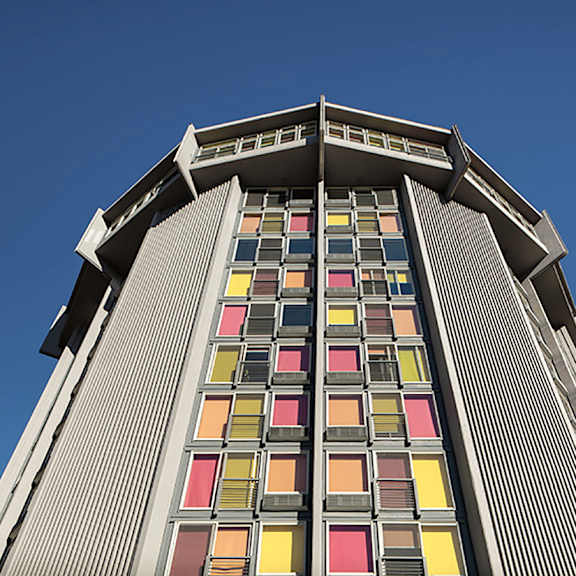 a tall building with a row of windows in red, yellow, orange, and pink.