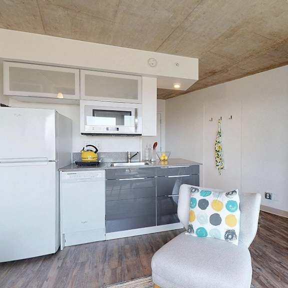 a white chair with a multicolored pillow sits in a kitchen with a white refrigerator and white cabinets.