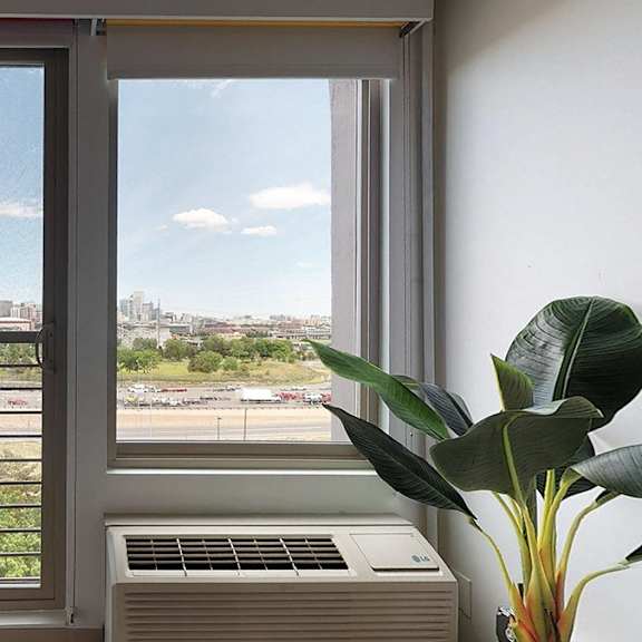 a view of a cityscape through a window with a blue cushion on the left and a plant on the right.
