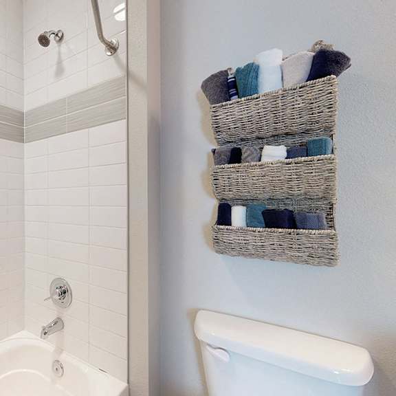 a white bathtub with a shower head and a basket of towels on the wall.