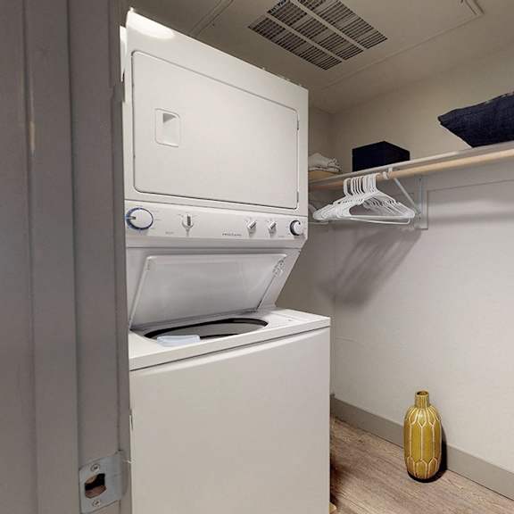 a yellow vase sits on the floor next to a white oven and dryer.