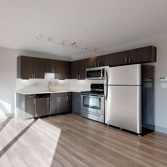 a modern kitchen with stainless steel appliances and wooden flooring.
