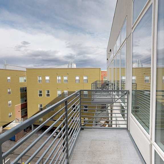 a balcony with a metal railing and glass windows overlooks a courtyard with a metal staircase.