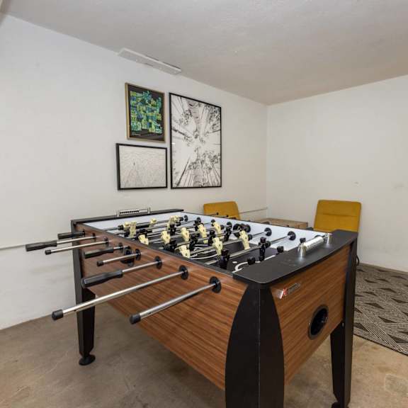 a foosball table sits in a room with a rug and two framed pictures on the wall.