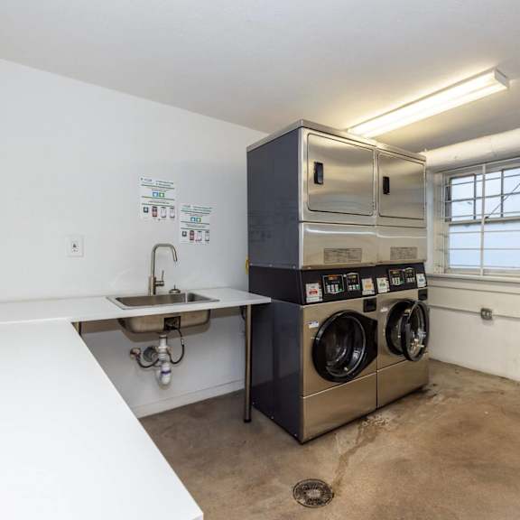 a laundry room with a washer and dryer, sink, and trash can.