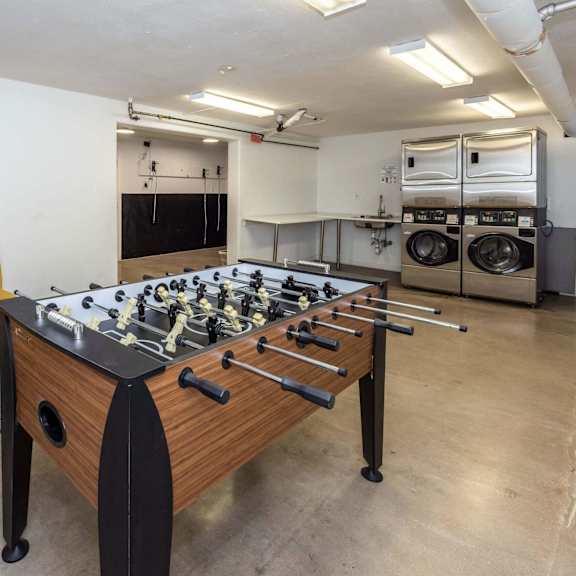 a foosball table is in the middle of a room with a yellow chair and a washing machine in the background.