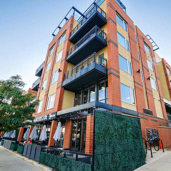 a multi-story building with balconies and a green fence in front.