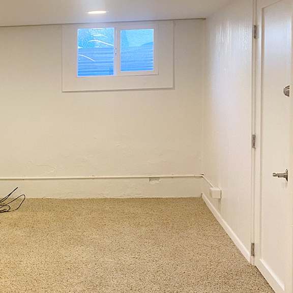a room with a carpeted floor, a window with blinds, and a door.