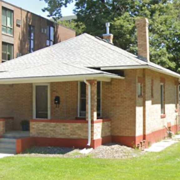 a small house with a red brick chimney sits in front of a large building.