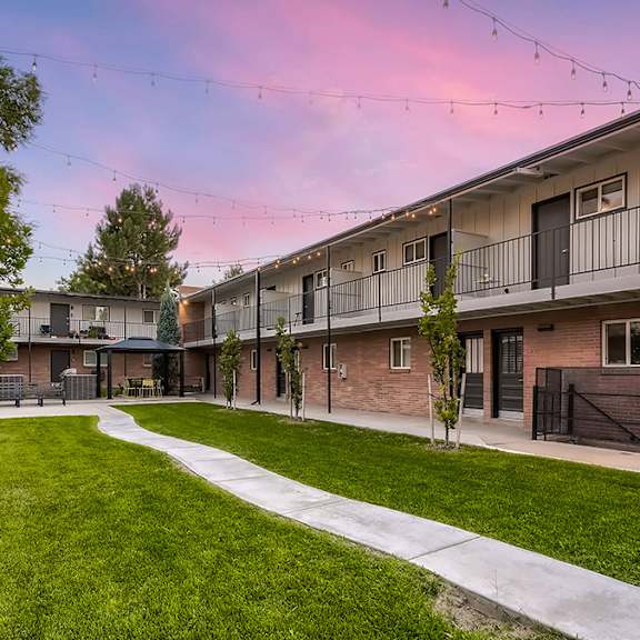 a sunset view of apartment buildings with a green lawn in the foreground.