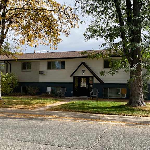 view of arvada trails apartment building from across the street. 2-story brick building with trees in front.