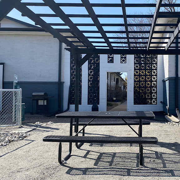 a picnic table and gas grill under a black pergola.