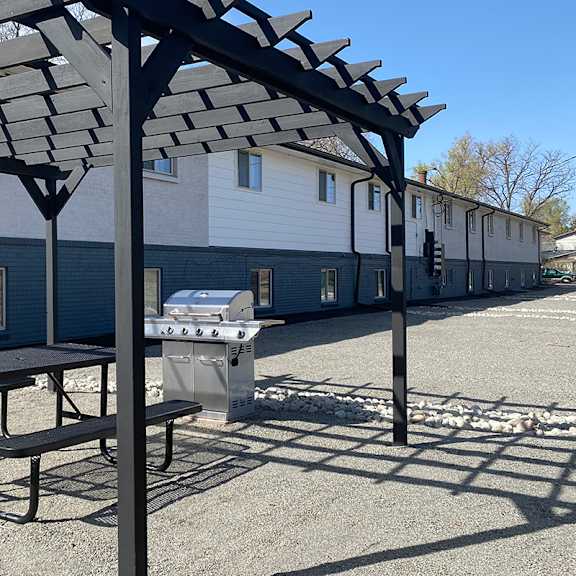 a picnic table and gas grill under a canopy on a gravel lot.