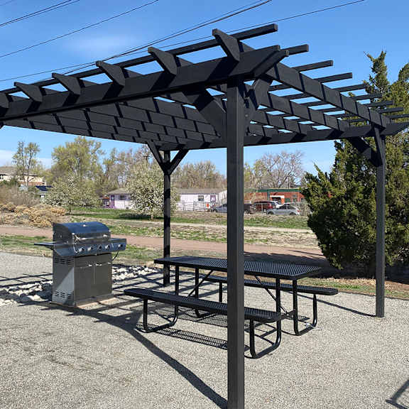 a black pergola with a picnic table and gas grill underneath it.