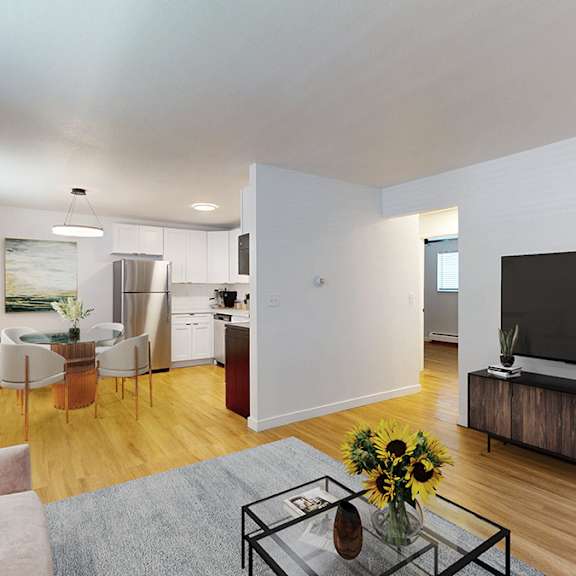 a modern living room with a sofa, a glass coffee table, and a television. dining table and kitchen visible in the background.