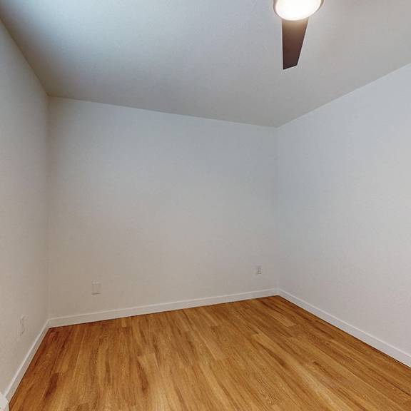 a room with a wooden floor and a window with blinds, and ceiling fan.