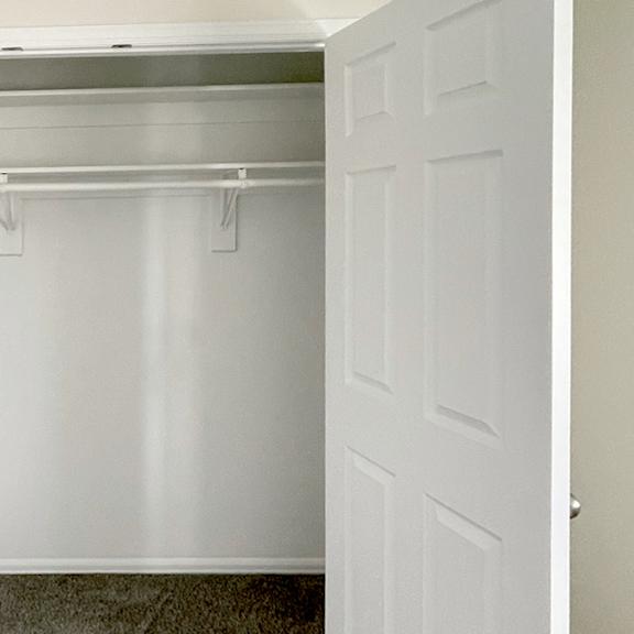 a white door is open to a small, empty room with a grey floor.