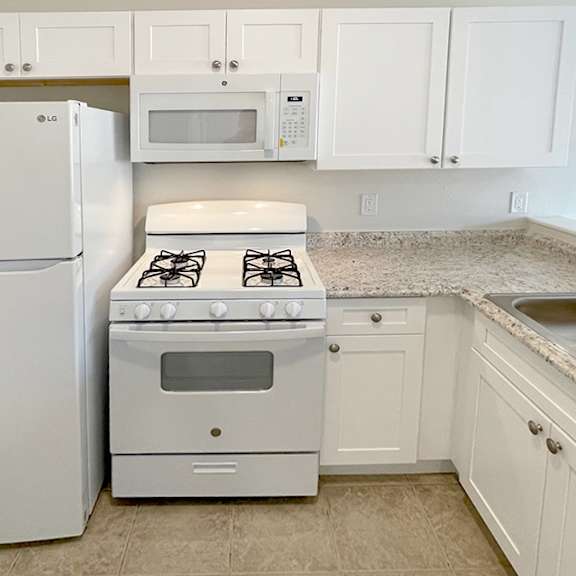 a white kitchen with a fridge, microwave, oven, and sink.