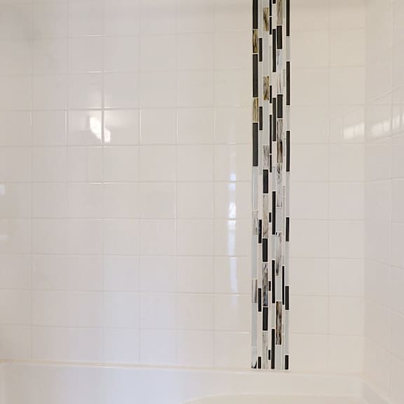 a white tiled shower with a black and white tile strip on the wall.