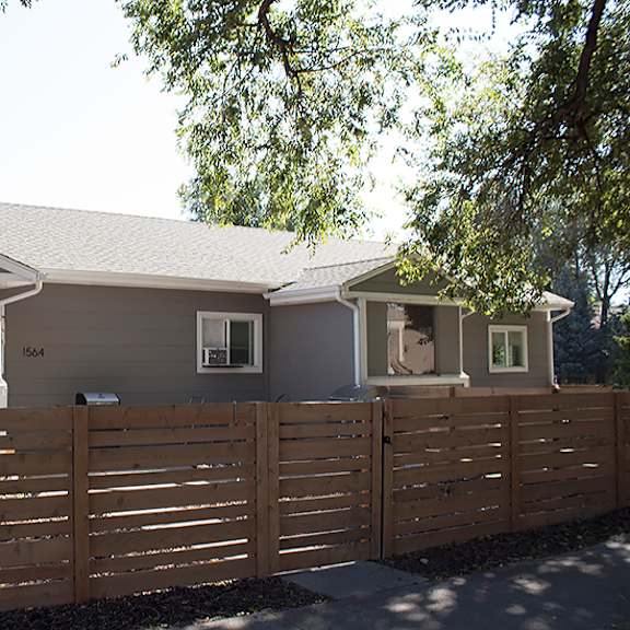 a house with a brown fence and a tree in front.