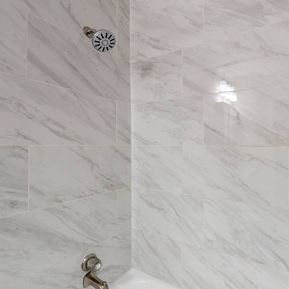a white tiled shower with a silver faucet.
