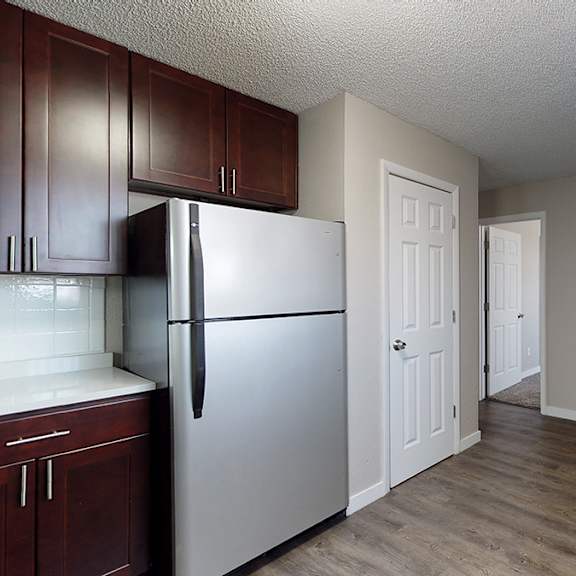 a kitchen with a refrigerator, cabinets, and a doorway leading to another room.