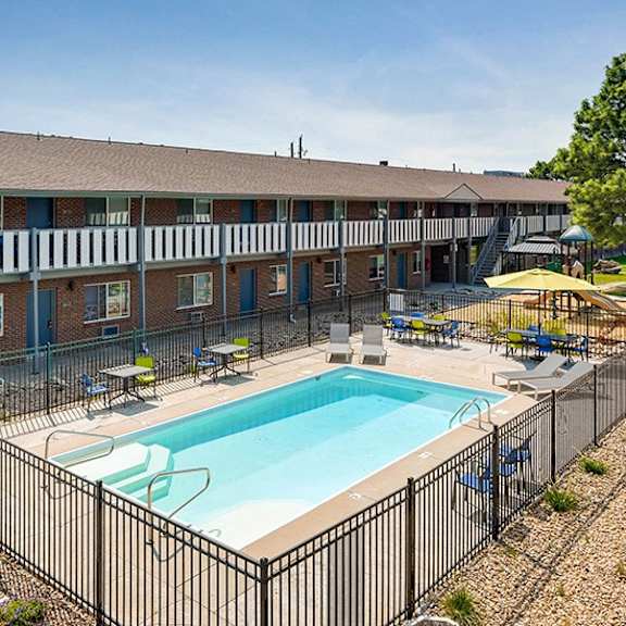 a black fence surrounds a small pool in front of a brick building.