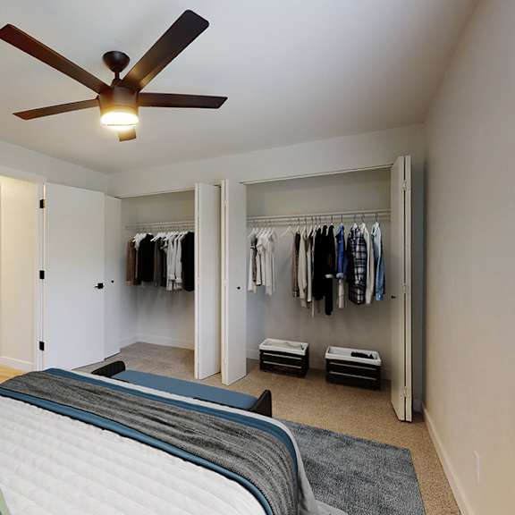 a bedroom with a bed, a ceiling fan, and a closet with clothes.