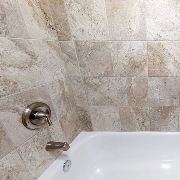 a white bathtub with a gold faucet in a tiled bathroom.