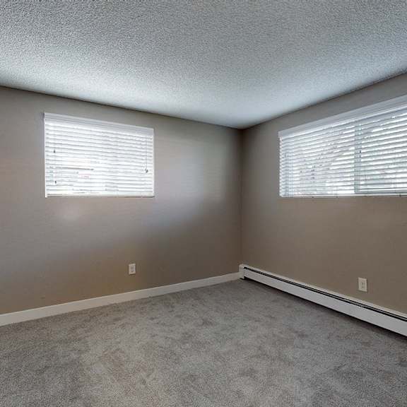 a room with carpeted floor and two windows with blinds.